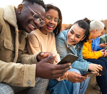 Young adults smiling while looking at a phone. 